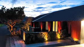 A house with a tiled roof, a porch with red curtains, and a garden with plants and a tree. - Limited to one pair per day! The entire building is reserved for private use! A luxurious inn designed in a modern Japanese style! You can enjoy your private time in the nature of Amami Oshima with a large projector. ⭐︎ (龍郷町)