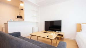 A modern, minimalist living room with a grey sofa, a wooden coffee table, a flat-screen TV, and a small wooden side table. - Felice Hakata (Fukuoka)