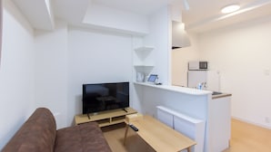 A compact living space with a sofa, a TV, a small kitchen area, and a dining table. - Felice Hakata (Fukuoka)