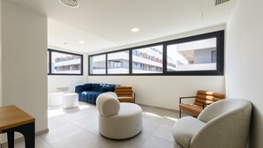 A modern living room with a sofa, two armchairs, a small table, and large windows offering a view of buildings. - Modern studio apartment with private terrace and excellent communal areas (San Sebastián de los Reyes)