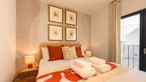A neatly made bed with a red and white blanket, two pillows, and a folded towel on the bed. There are framed pictures on the wall above the bed.