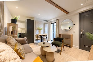 Un salon moderne avec un canapé, une table ronde et un fauteuil. On aperçoit à l’arrière-plan un coin repas avec une table et des chaises.