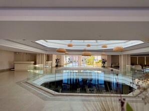 A spacious lobby with a central glass-bottomed pool, a reception desk, and a modern ceiling design. - Rosetta Hotel & SPA (Sharm El Sheikh)