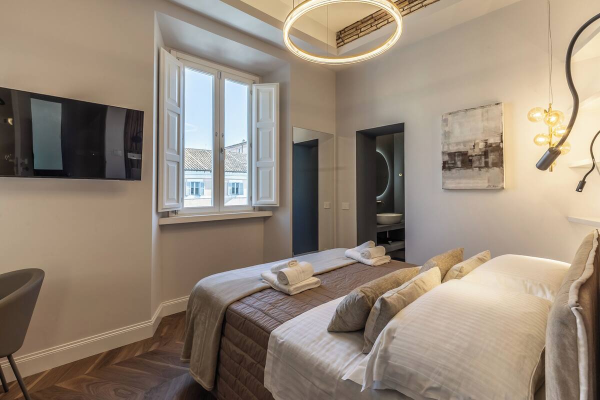 A modern hotel room with a large bed, a desk, a chair, and a TV mounted on the wall.
