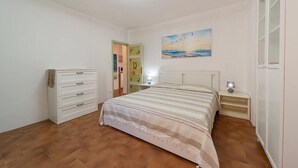 A bedroom with a bed, a dresser, a nightstand, a painting, and a door leading to another room.