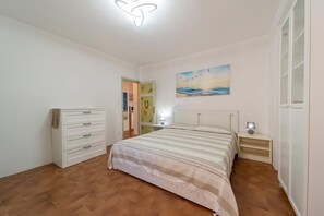 A bedroom with a bed, a dresser, a nightstand, a painting, and a door leading to another room.