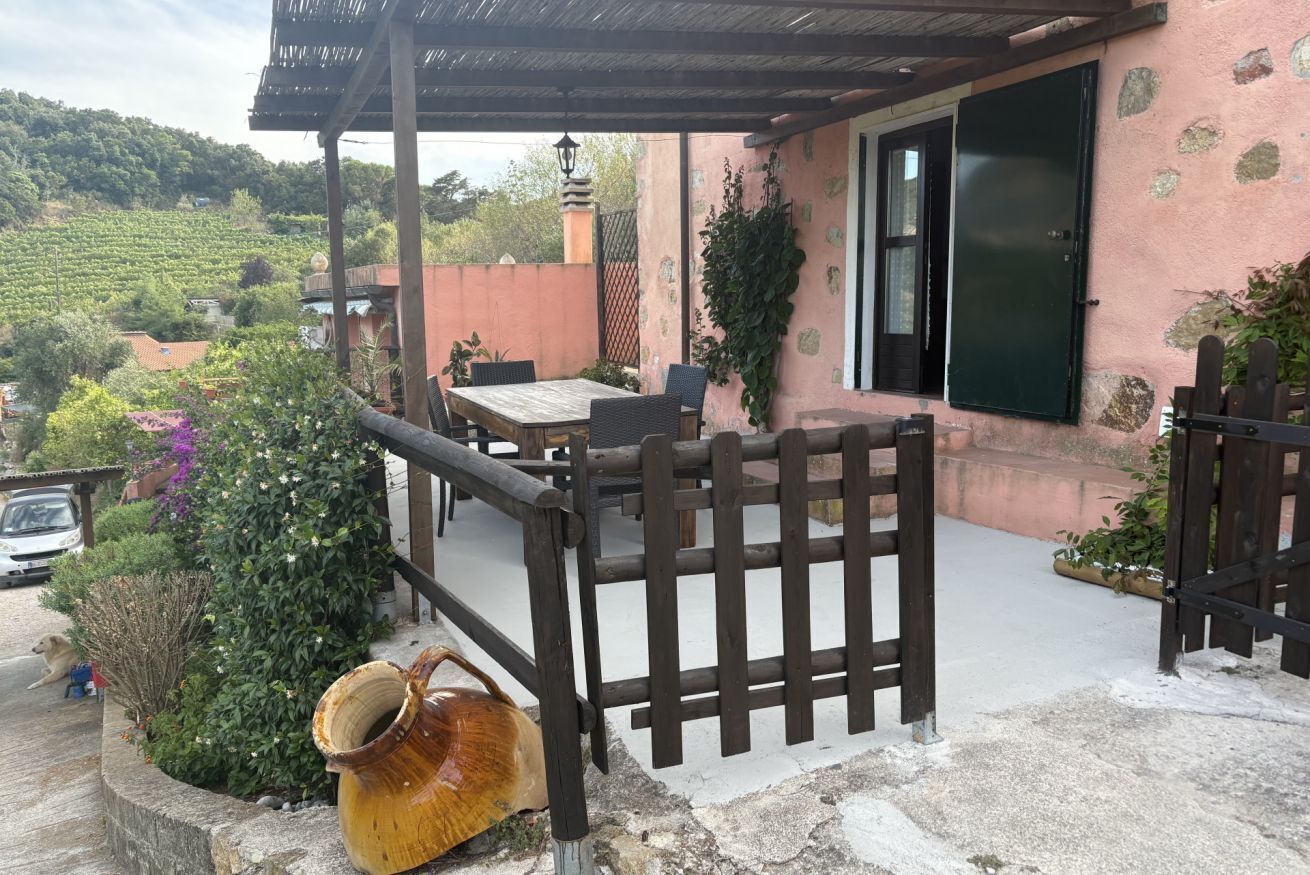 Um alpendre coberto com mesa e cadeiras, um portão de madeira e um vaso rústico.