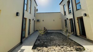 A courtyard with two-story buildings, a small tree, and a dry, cracked ground.
