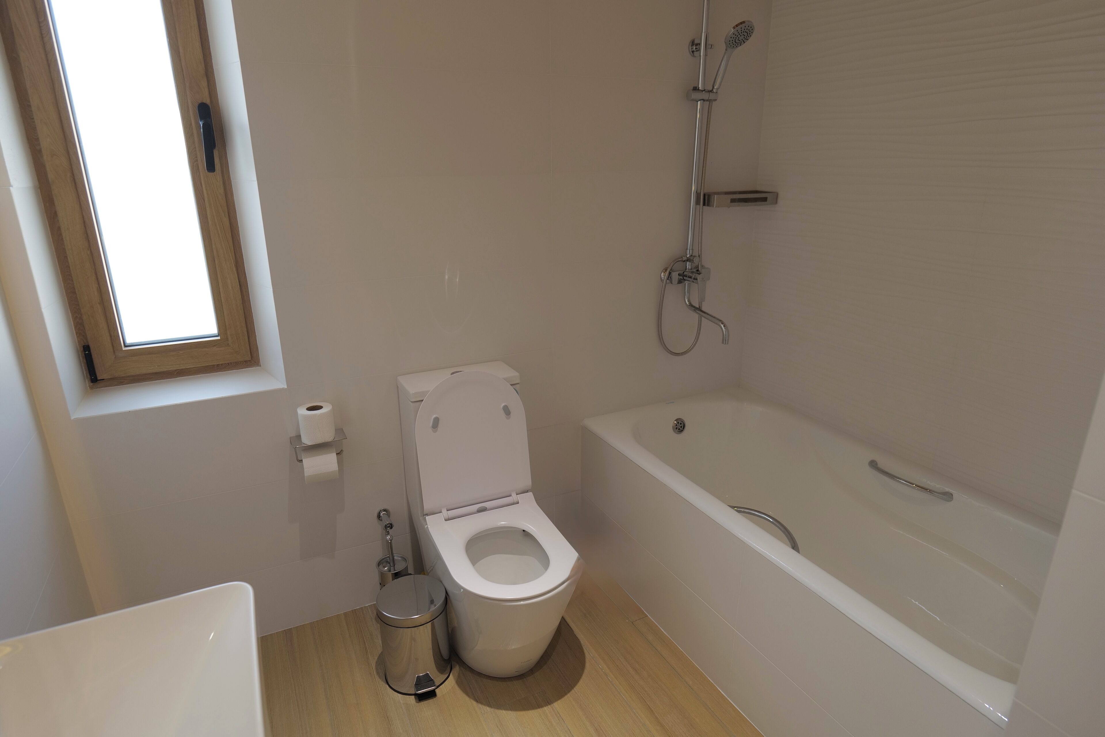 A bathroom with a toilet, a trash can, a bathtub, and a window.