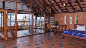 A room with a bed, a table, chairs, and a view of the sea.