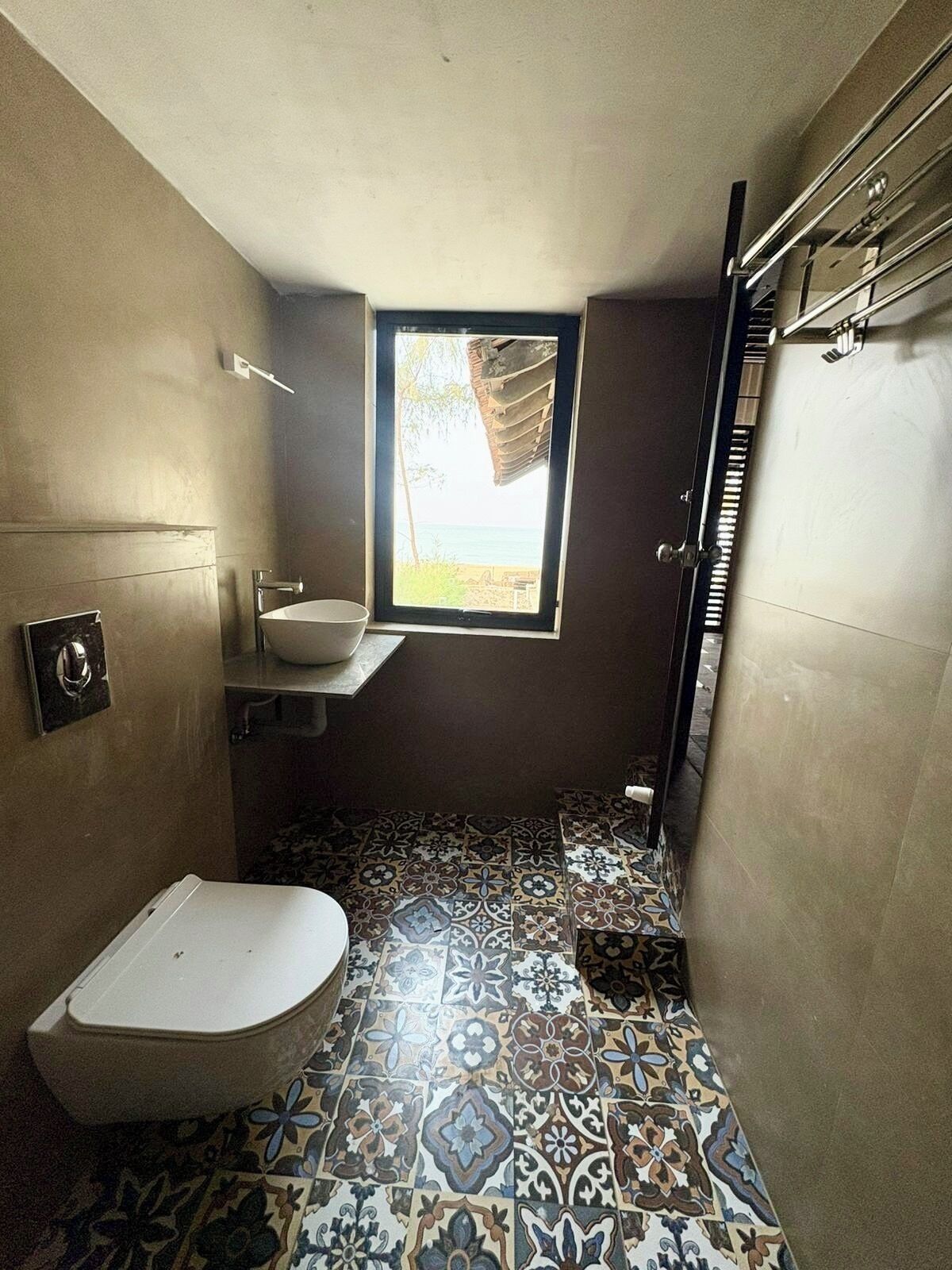 Un baño con inodoro, lavabo y ventana con vistas a la playa.