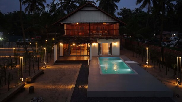 A two-story house with a swimming pool, surrounded by palm trees.