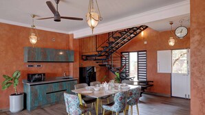 A dining area with a wooden staircase, a kitchen with teal cabinets, and a ceiling fan.