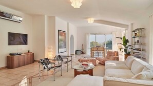 A spacious living room with a sofa, armchair, and a coffee table. There is a television mounted on the wall, a guitar, and a plant. - Villa Casa Rosetta A/C avec Piscine & Jacuzzi  -Vallauris (Vallauris)