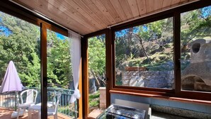 A room with a gas stove, a glass table, a chair, and a view of a garden through large windows. - Casa Greta, just a few steps from the sea (Sant'Andrea)