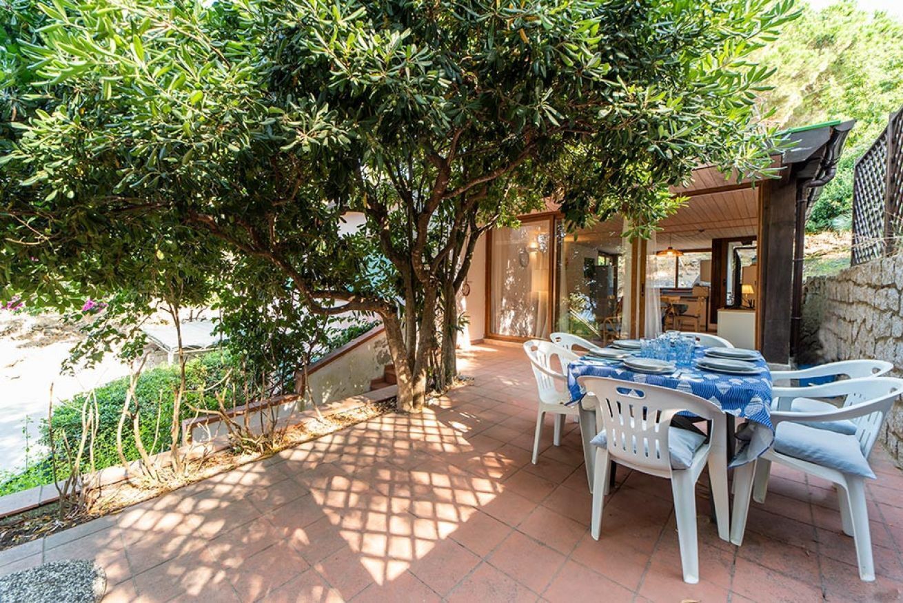 Une terrasse extérieure avec une table et des chaises, entourée d’arbres et d’un mur en pierre.