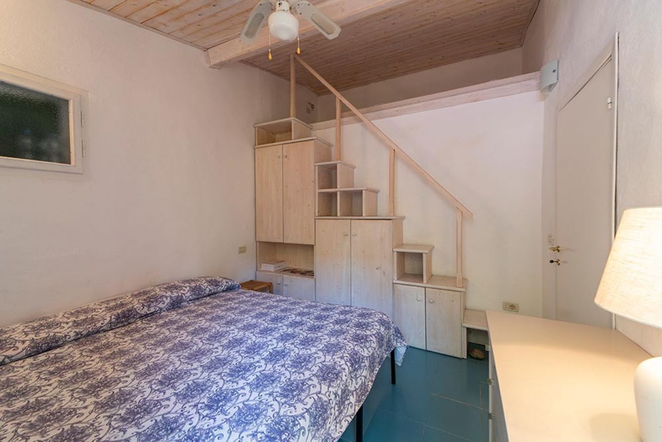 Une chambre à coucher avec un lit, un escalier en bois et un ventilateur de plafond.