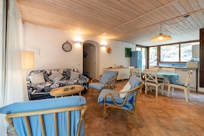 A cozy living room with a sofa, chairs, a dining table, and a kitchen area.