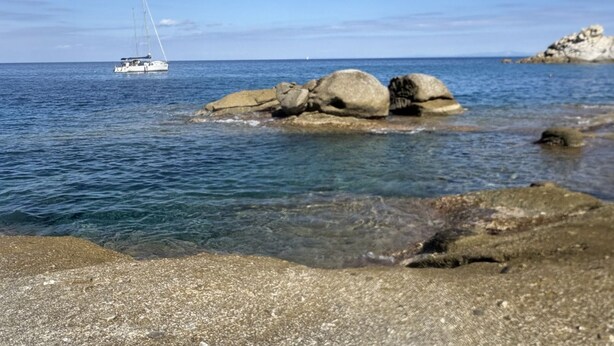 A coastal scene with a sailboat on the water and large rocks in the foreground. - Casa Greta, just a few steps from the sea (Sant'Andrea)
