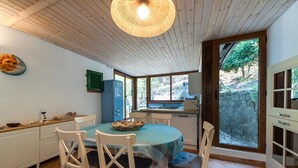 A kitchen with a dining table, chairs, a hanging light fixture, and a view of a stone wall outside. - Casa Greta, just a few steps from the sea (Sant'Andrea)