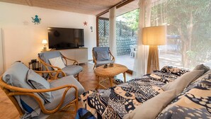 A living room with wicker furniture, a television, and a large window with a view of greenery. - Casa Greta, just a few steps from the sea (Sant'Andrea)