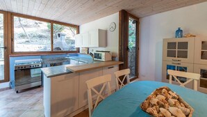 A compact kitchen with a stove, sink, and a dining area with a table and chairs. - Casa Greta, just a few steps from the sea (Sant'Andrea)