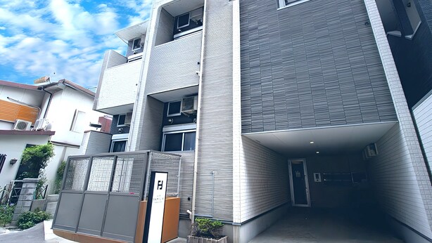 A modern multi-story building with a covered entrance, air conditioning units, and a gated area. - HOTEL FAMILIA Hakata East (Fukuoka)