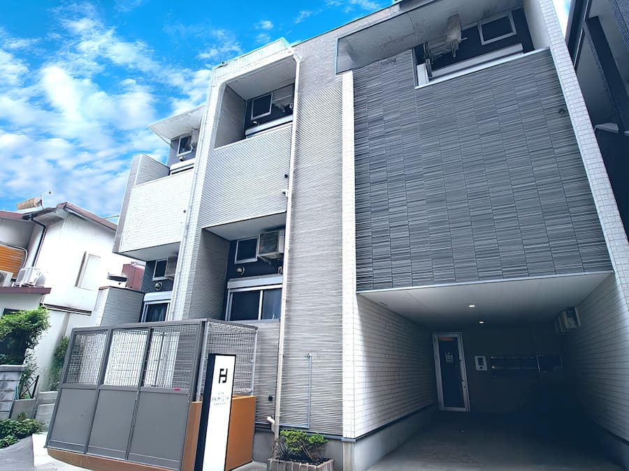 Um edifício moderno de vários andares com entrada coberta, unidades de ar condicionado e área cercada.