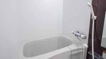Uma banheira branca com chuveiro manual, um pequeno prateleira e um espelho.