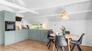 A modern kitchen with a dining area, featuring a large window, wooden flooring, and a hanging light fixture.
