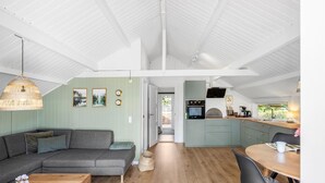 A modern interior with a grey sofa, wooden dining table, and a kitchen area with a built-in oven and microwave.