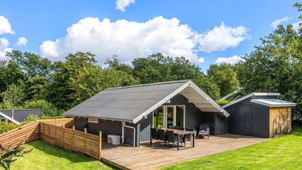 A modern cabin with a deck, a dining area, and a small attached shed.