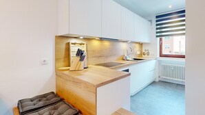 Une cuisine moderne dotée d’un plan de travail en bois, d’un bloc à couteaux encastré et d’une fenêtre avec des stores.
