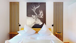 Une chambre à coucher moderne avec un grand lit, du linge de lit blanc et un tableau représentant la tête d’un cerf, accroché au mur.