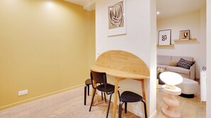 Ein Essbereich mit Holztisch und Stühlen, einem kleinen runden Tisch mit Lampe und einer Couch im Hintergrund.