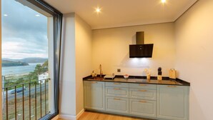 A modern kitchen with a large window overlooking a scenic view, a built-in oven, and a range hood. - Sea View - 2 Bedrooms - Pet Friendly - Ideal for Families - Noia (Noia)