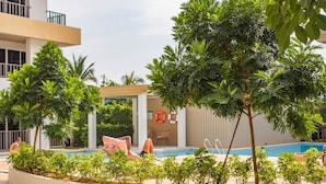 Zona de piscina con sillas de descanso y un pequeño edificio, rodeada de vegetación.