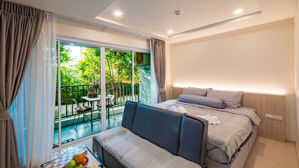 Una habitación de hotel moderna con balcón, una cama, un sofá y una pequeña mesa con frutas y flores.