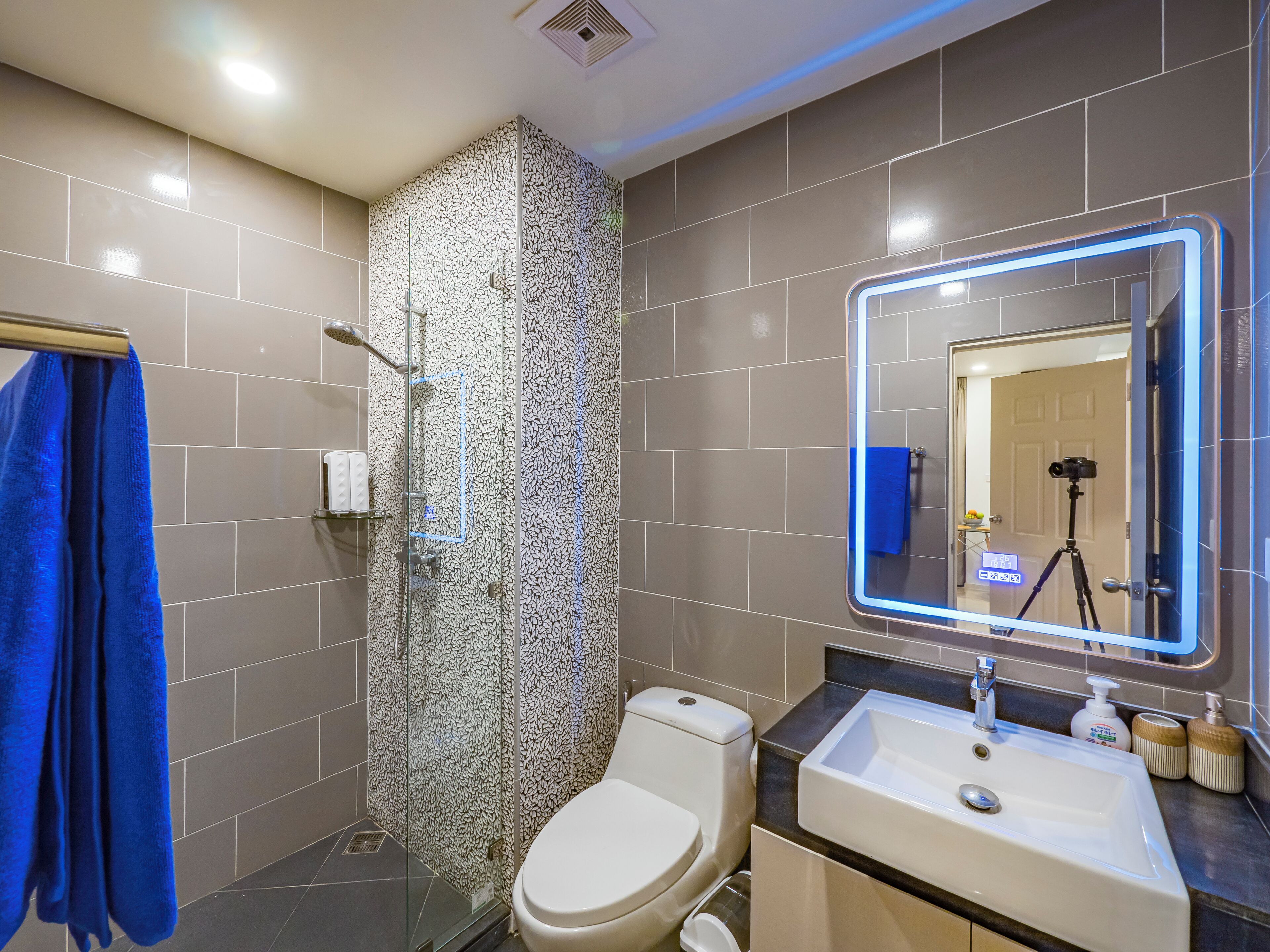 A modern bathroom with a glass shower enclosure, a toilet, a sink with a mirror, and a blue towel hanging on a rack.