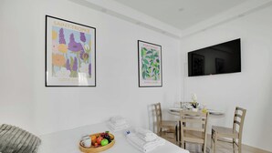 Une chambre d’hôtel comprenant un lit, une table à manger avec des chaises, un téléviseur fixé au mur et deux tableaux encadrés accrochés au mur.