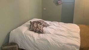 Ett sovrum med en säng, en liten pall och ett fönster med gardiner.