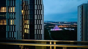 A modern building with a balcony overlooking a cityscape at dusk.