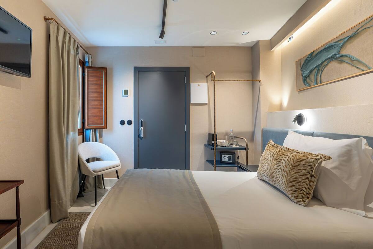 Een hotelkamer met een bed, een stoel, een bureau met een lamp, een televisie en een deur.