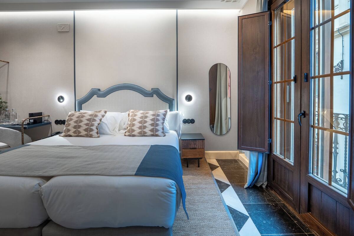 Een moderne hotelkamer met een groot bed, nachtkastjes, een spiegel en een garderobe met glazen deuren.