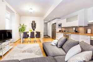 A modern living room with a grey sofa, a flat-screen TV, and a dining area with a table and chairs. - Practical & Spacious 2-Bedroom Apartment w/ Private Sauna in Central Helsinki (Helsinki)
