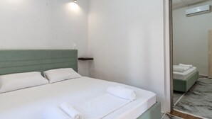 A neatly made bed with white linens and rolled towels, a green headboard, a small bedside table, and a mirror reflecting part of the room. - Country House 'Azure Nest' with Private Terrace, Wi-Fi, and Air Conditioning (Nea Peramos)