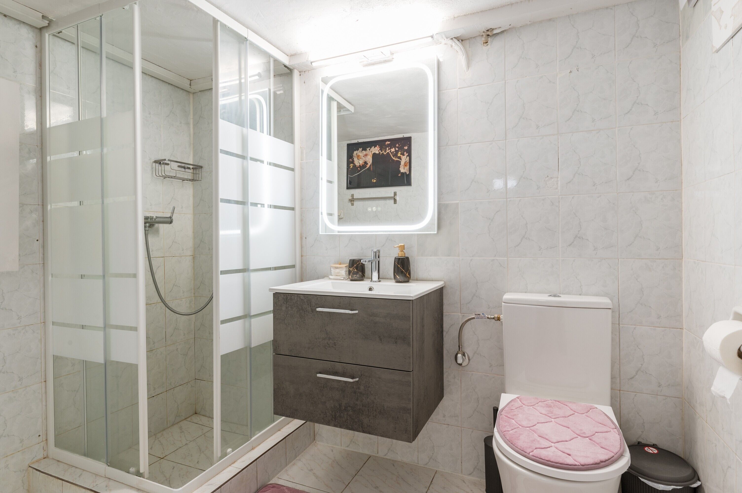 Ein Badezimmer mit einer Duschkabine, einem Waschtisch mit Spiegel und einer Toilette.