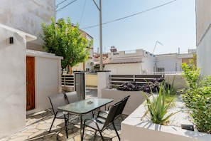 Eine Terrasse im Freien mit Tisch und Stühlen, umgeben von Pflanzen und einer weißen Mauer.