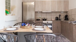 A modern kitchen with wooden cabinets, a stainless steel refrigerator, and a dining table set for two. - Country House 'Azure Nest' with Private Terrace, Wi-Fi, and Air Conditioning (Nea Peramos)