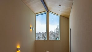 A staircase with a wooden handrail, a ceiling with recessed lighting, and a view of snow-covered trees through two windows. - Sakuraya (Hakuba)